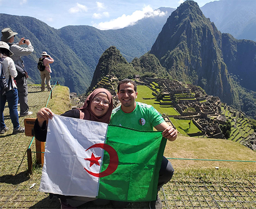 Hadjer and Mokhtar pose in front of Machu Picchu holding Algerian flag